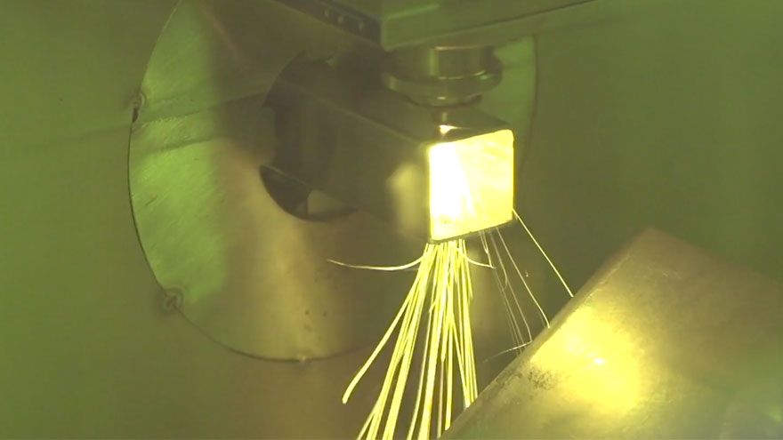 A fiber laser tube cutting machine with sparks flying below where the cut is being made